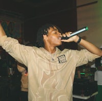 a man in a tan sweatshirt singing into a microphone
